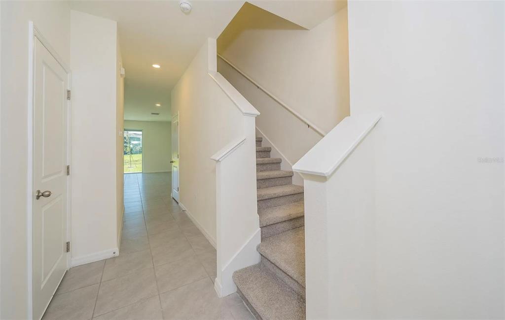 An interior view shows a tiled hallway leading to a doorway and carpeted stairs — 1623 HUBBELL ROAD, WESLEY CHAPEL, FL