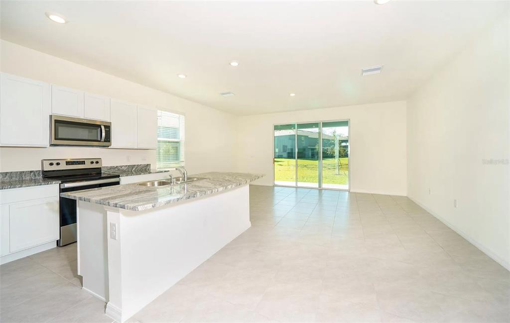 A kitchen with white cabinets and a granite island opens into a spacious tiled living area — 1623 HUBBELL ROAD, WESLEY CHAPEL, FL