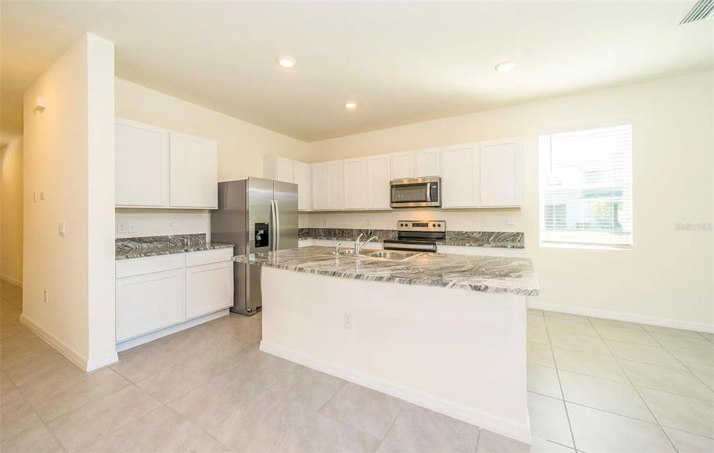 A kitchen features white cabinets, granite countertops, stainless steel appliances, and light-colored tile flooring — 1623 HUBBELL ROAD, WESLEY CHAPEL, FL