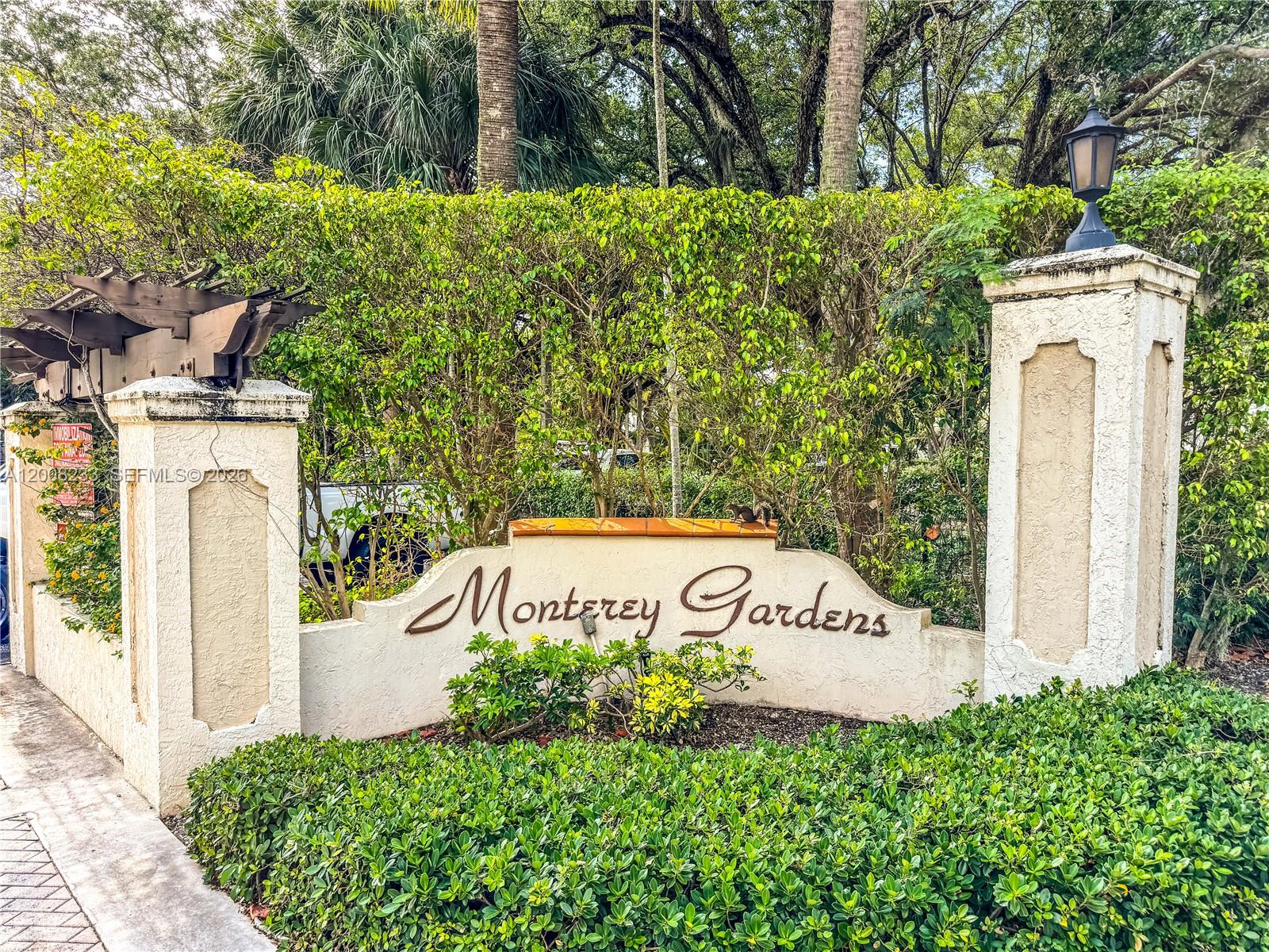 A stucco entrance sign for Monterey Gardens features a wooden pergola and a small squirrel — 8605 SW 68th Ct # 7, Pinecrest FL 33156, PINECREST, FL
