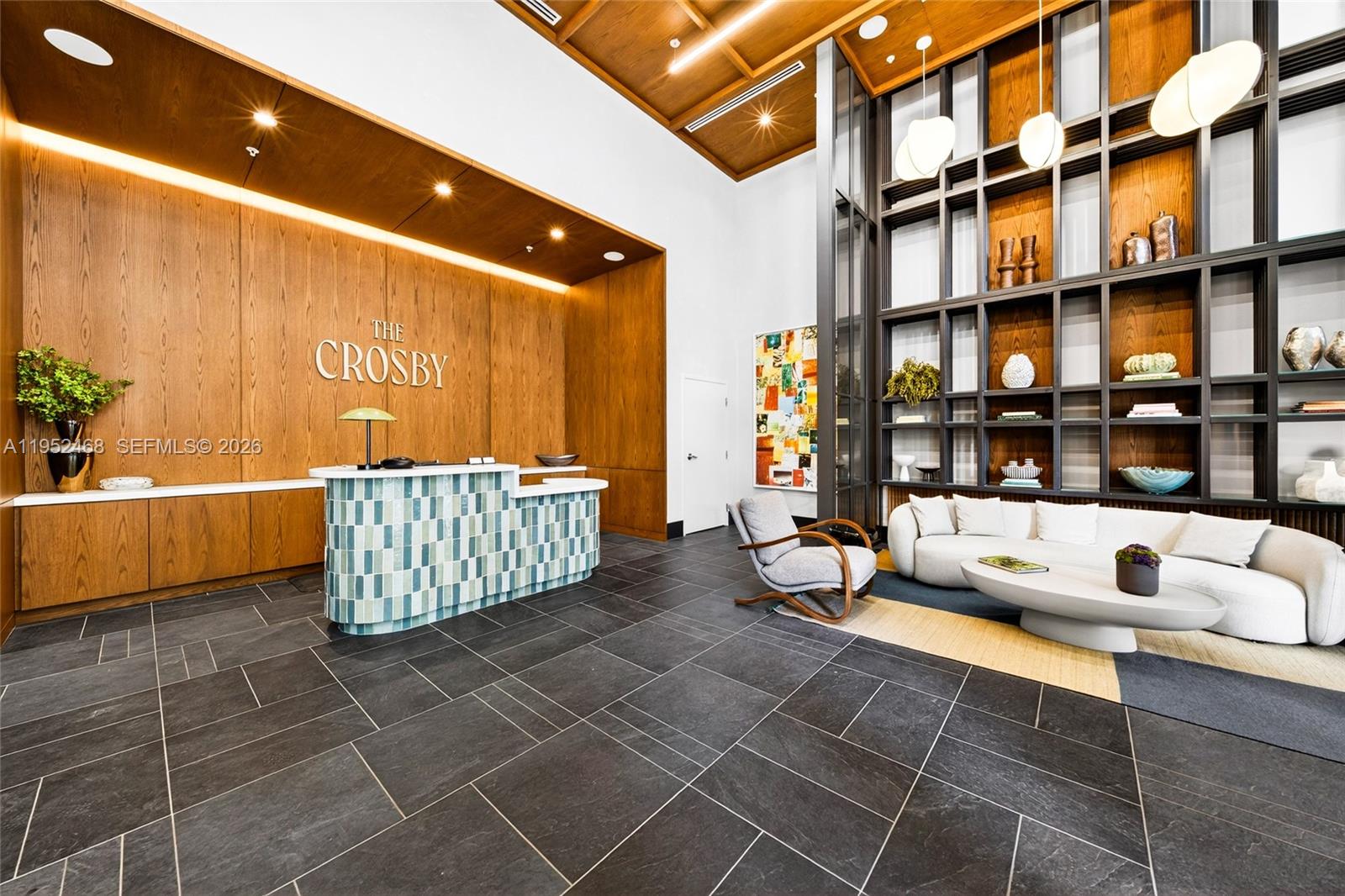 A modern lobby features a wood-paneled reception desk, dark tile flooring, and a large shelving unit — 11 NE 6 ST # 3210, Miami FL 33132, MIAMI, FL