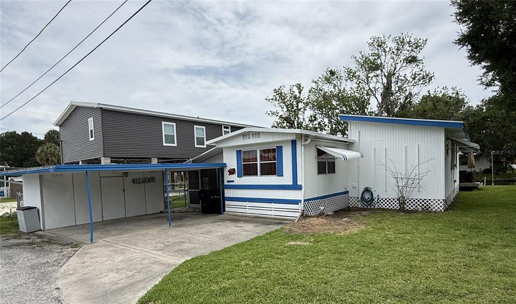 A white mobile home with blue trim and an attached carport sits on a lawn — 10270 W GROTTO COURT, HOMOSASSA, FL