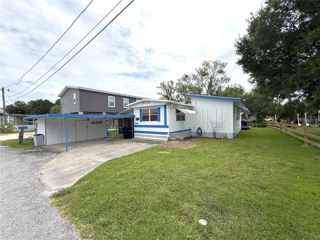 A white mobile home with blue trim and an attached carport sits on a grassy lot — 10270 W GROTTO COURT, HOMOSASSA, FL