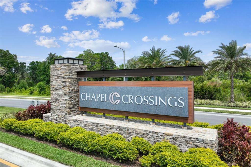 A stone and wood monument sign for Chapel Crossings stands beside a paved road — 5639 MAYDALE AVENUE, WESLEY CHAPEL, FL
