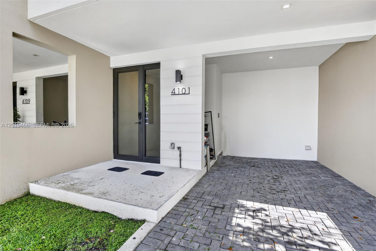 A modern home entrance features a glass door, white siding, and a paved driveway — 4101 N Oak Pl, Dania Beach FL 33314, DANIA BEACH, FL