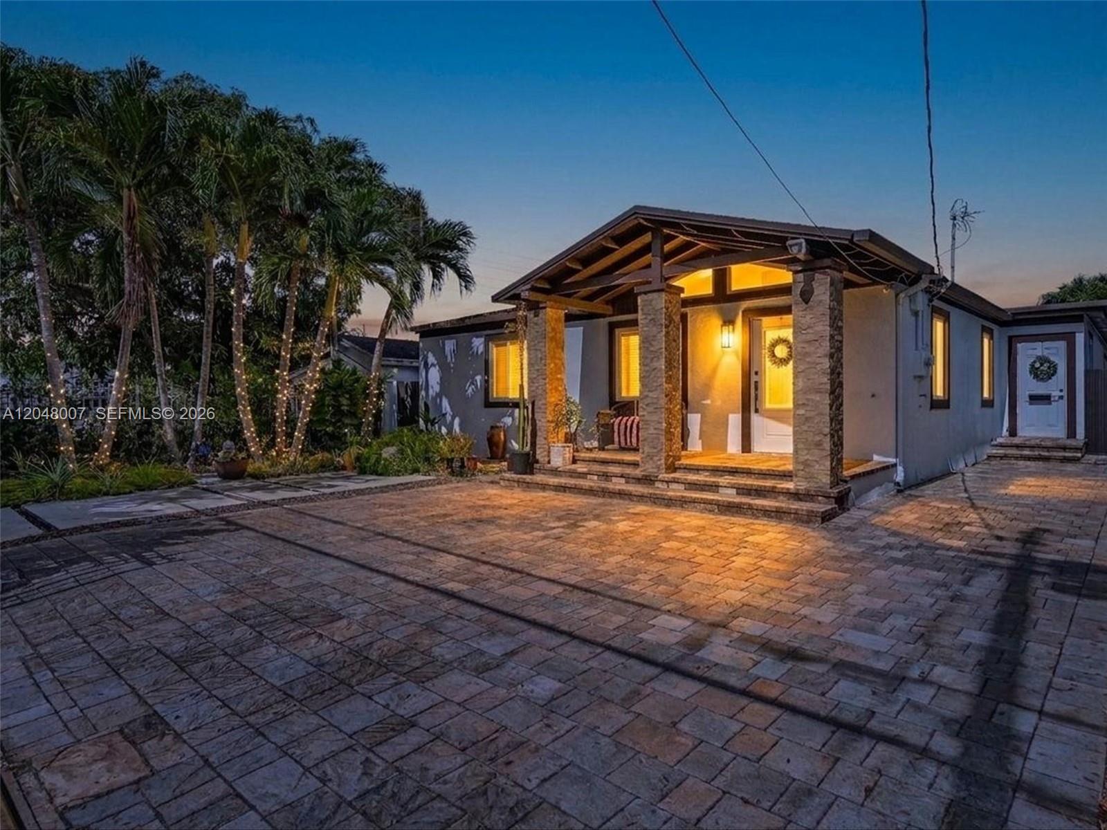 A single-story house with a stone-pillared porch and a paved driveway at dusk — 310 SW 65th Ave, Miami FL 33144, MIAMI, FL