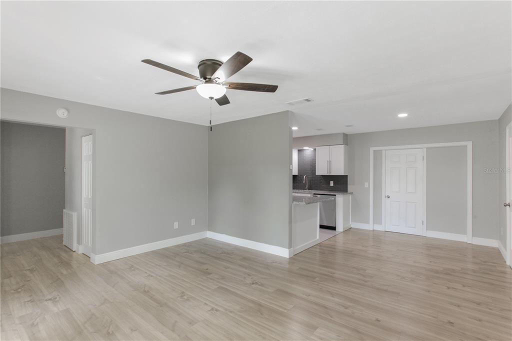 A living area with light wood-look flooring, gray walls, and an open kitchen beyond — 1022 NORWOOD DRIVE, DELTONA, FL