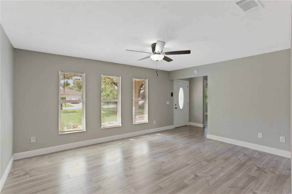 A living room with light gray walls, wood-look flooring, three windows, and a ceiling fan — 1022 NORWOOD DRIVE, DELTONA, FL