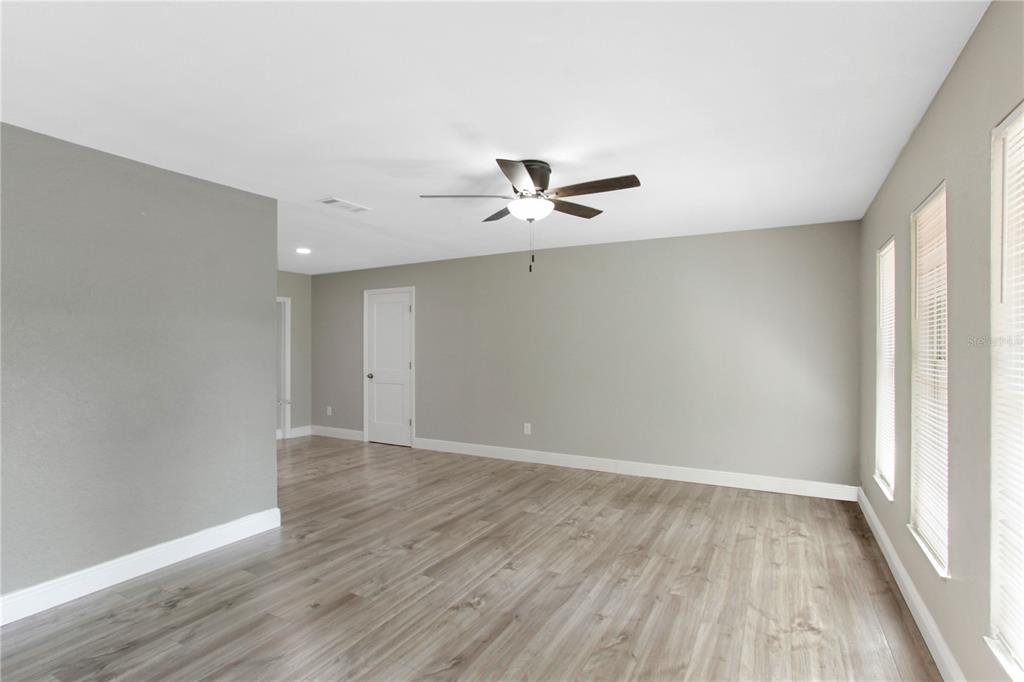 An empty room features light gray walls, wood-look flooring, a ceiling fan, and three windows — 1022 NORWOOD DRIVE, DELTONA, FL