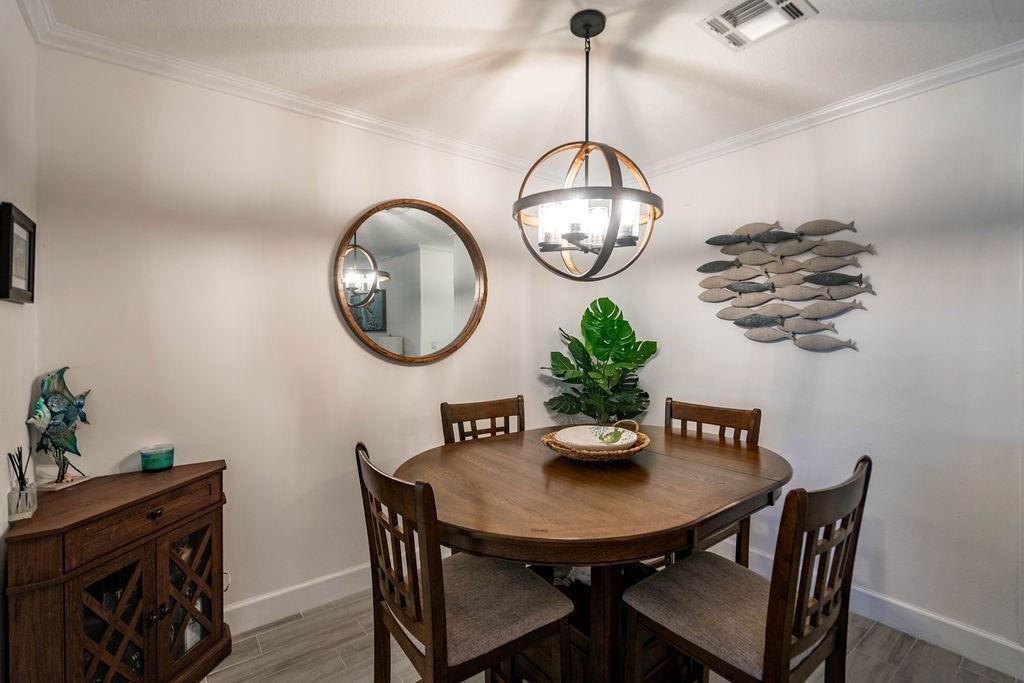 A dining area features a round wooden table, four chairs, a chandelier, and coastal wall decor — 2100 NE 38th Street # 229, Lighthouse Point FL 33064, LIGHTHOUSE POINT, FL