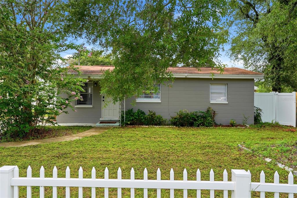 A single-story gray house with a white front door sits behind a white picket fence — 2430 N RAMONA CIRCLE, TAMPA, FL