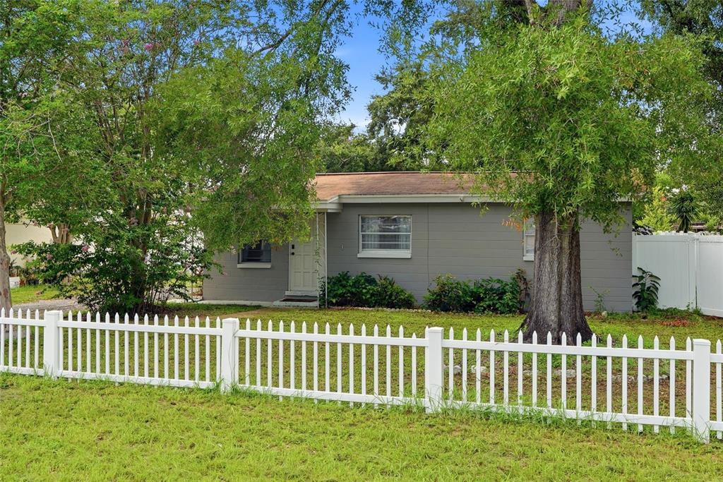 A gray single-story house sits behind a white picket fence surrounded by mature trees — 2430 N RAMONA CIRCLE, TAMPA, FL
