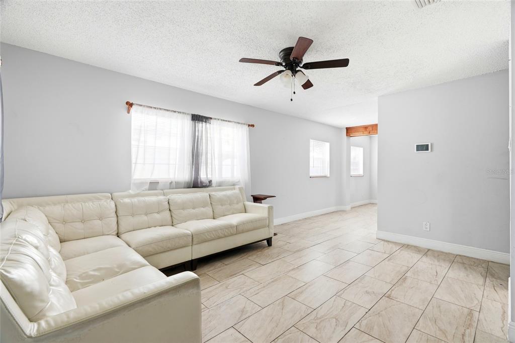 A living room features a white sectional sofa, light-colored tile flooring, and a ceiling fan — 2430 N RAMONA CIRCLE, TAMPA, FL