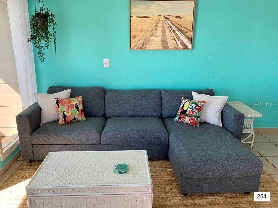A living room features a gray sectional sofa, a white coffee table, and turquoise walls — 2506 N ROCKY POINT DRIVE UNIT 254, TAMPA, FL