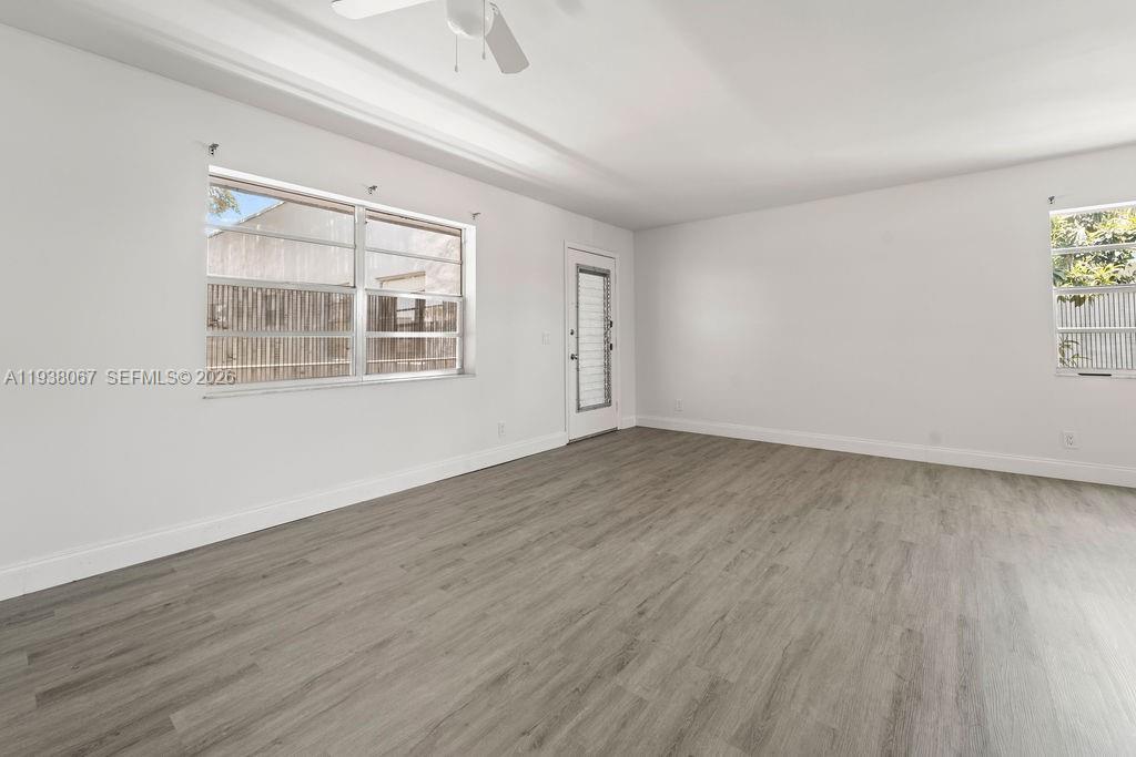 An empty room features white walls, gray wood-look flooring, a ceiling fan, and two windows — 938 Normandy T # T938, Delray Beach FL 33484, DELRAY BEACH, FL