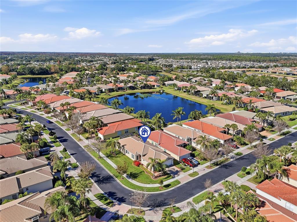 An aerial view shows a residential neighborhood with houses surrounding a central pond — 15767 CRYSTAL WATERS DRIVE, WIMAUMA, FL
