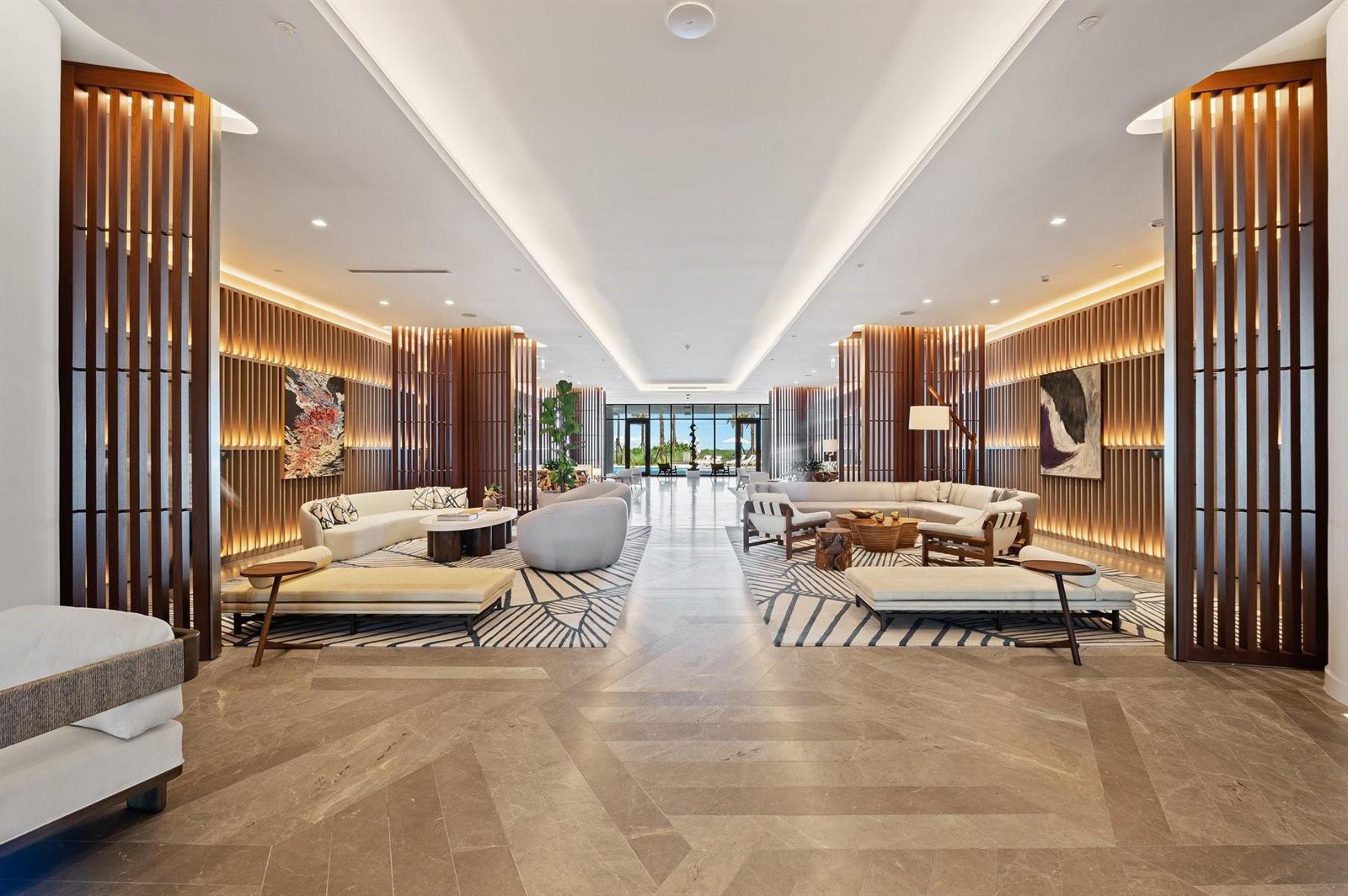 A spacious hotel lobby features symmetrical seating areas, wood-slatted wall panels, and stone flooring — 1116 N Ocean Boulevard # 1606, Pompano Beach FL 33062, POMPANO BEACH, FL