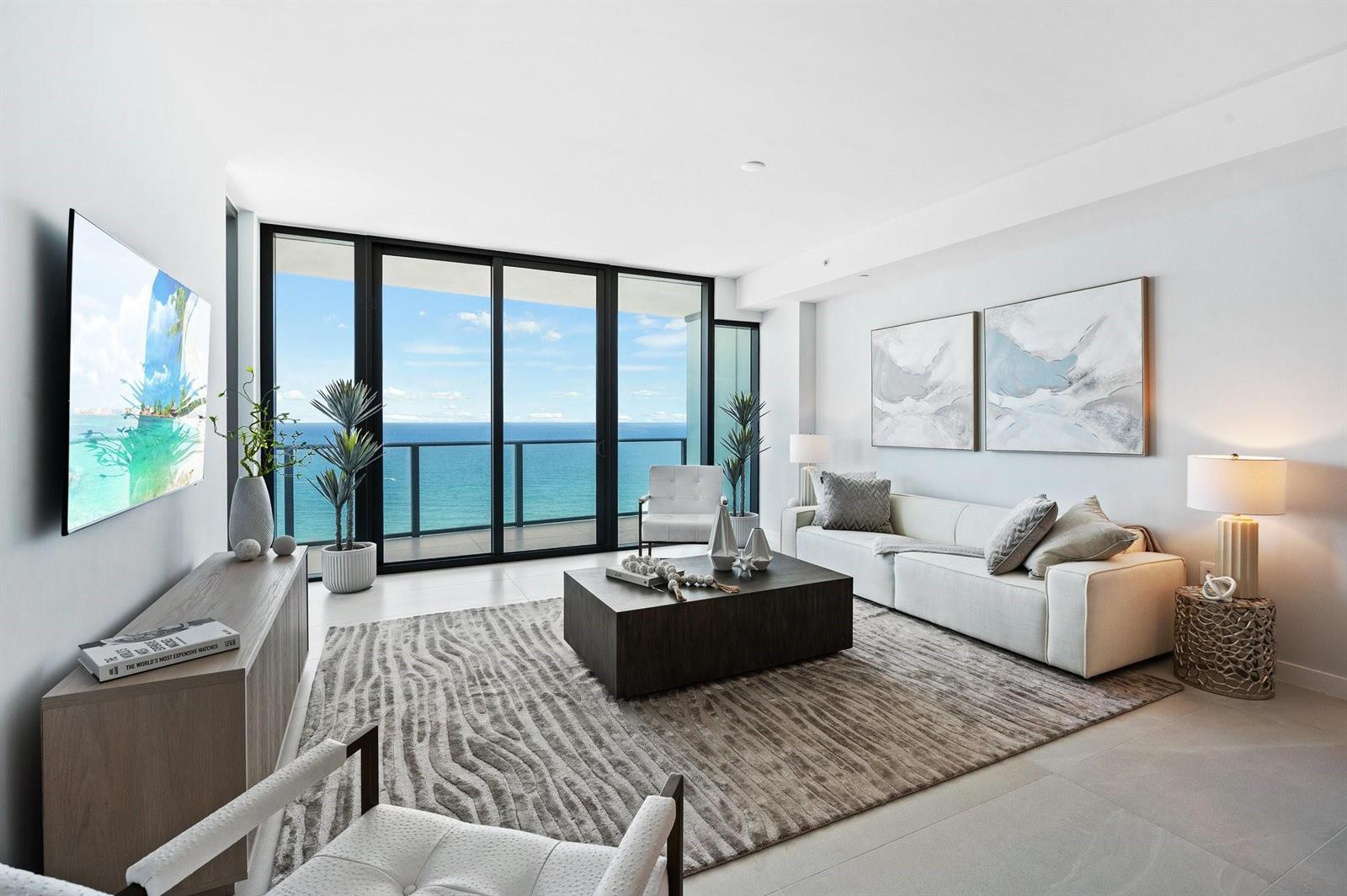 A modern living room features a white sofa, coffee table, and floor-to-ceiling windows overlooking ocean — 1116 N Ocean Boulevard # 1606, Pompano Beach FL 33062, POMPANO BEACH, FL