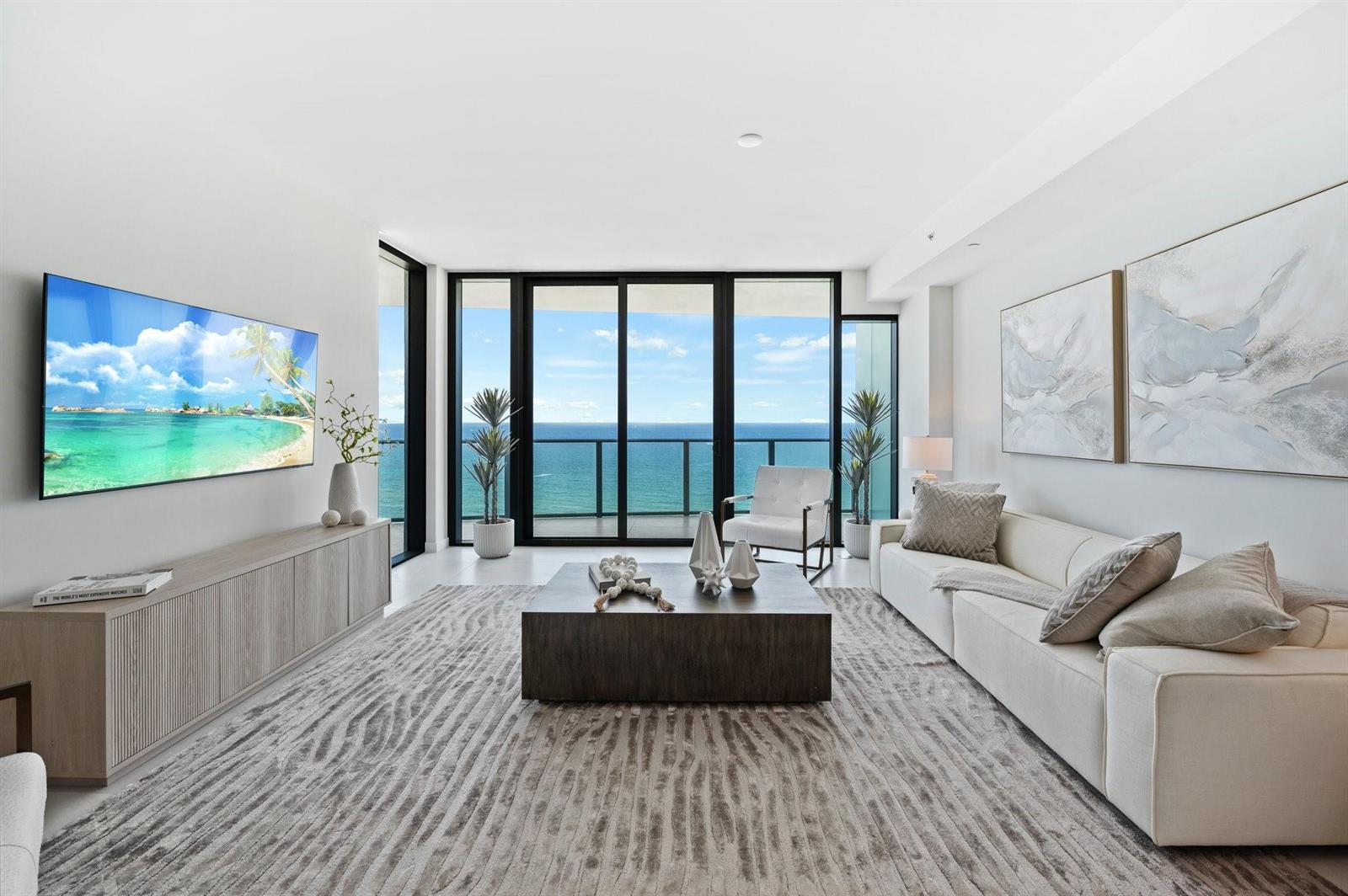 A modern living room features a large sofa, coffee table, and floor-to-ceiling ocean view windows — 1116 N Ocean Boulevard # 1606, Pompano Beach FL 33062, POMPANO BEACH, FL