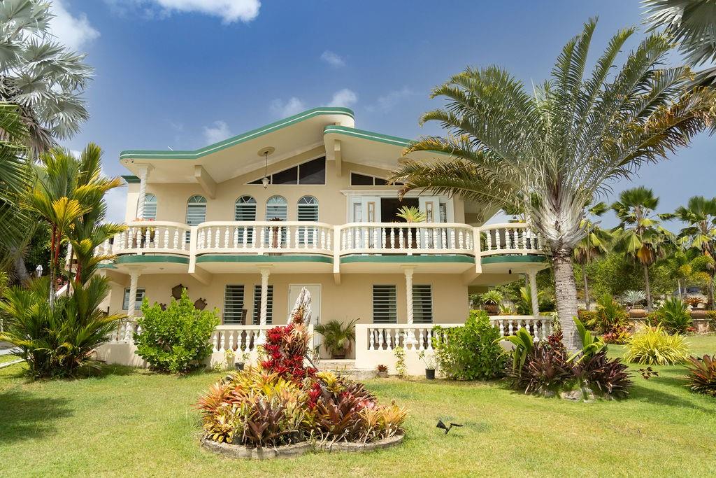 A two-story beige house with a balcony and palm trees in a grassy yard — 393 MONTE CARMELO, VIEQUES, PR