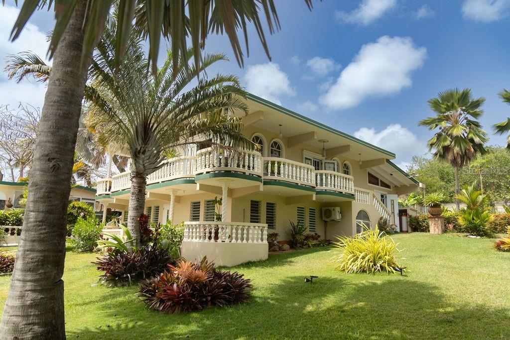 A two-story house with a wrap-around balcony and white railings sits on a grassy lawn — 393 MONTE CARMELO, VIEQUES, PR