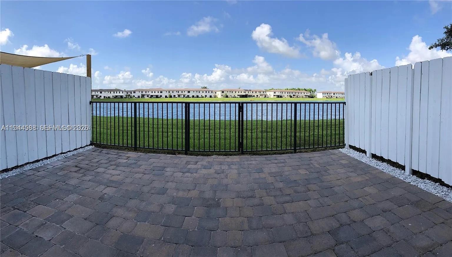 A paved patio features a black metal fence overlooking a lake and residential buildings — 10162 SW 228th Ter, Miami FL 33190, MIAMI, FL