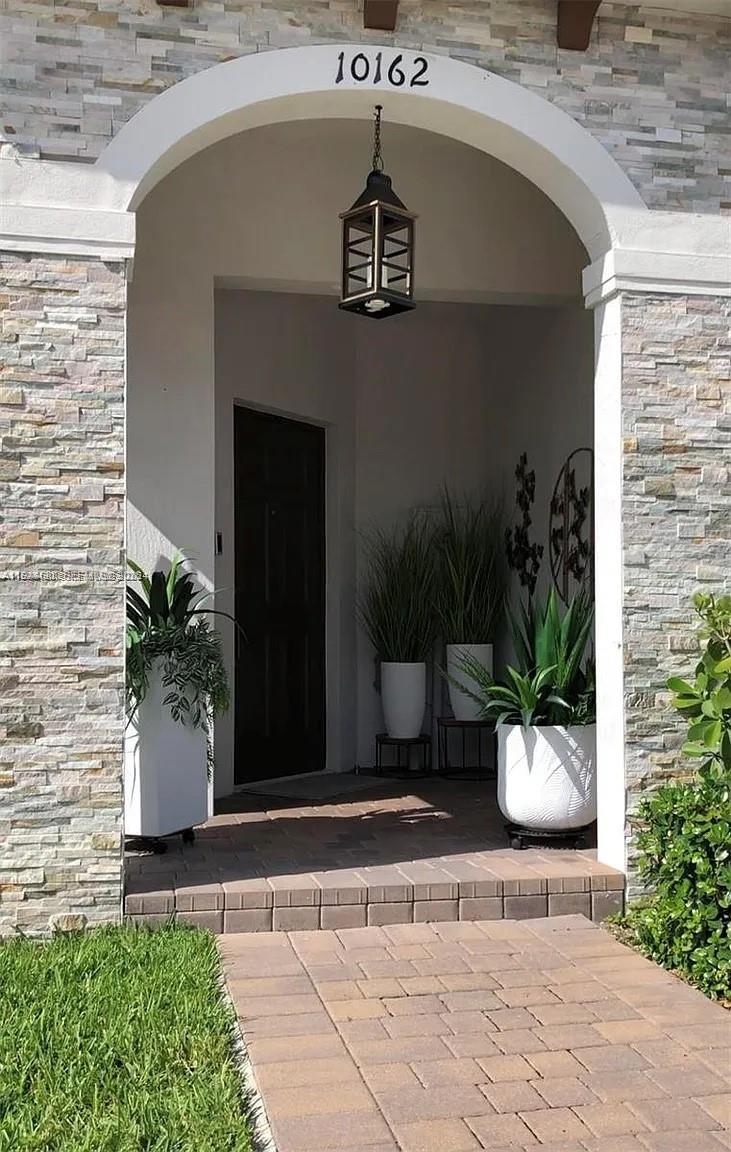An arched entryway features stone veneer walls, a hanging lantern, and potted plants — 10162 SW 228th Ter, Miami FL 33190, MIAMI, FL