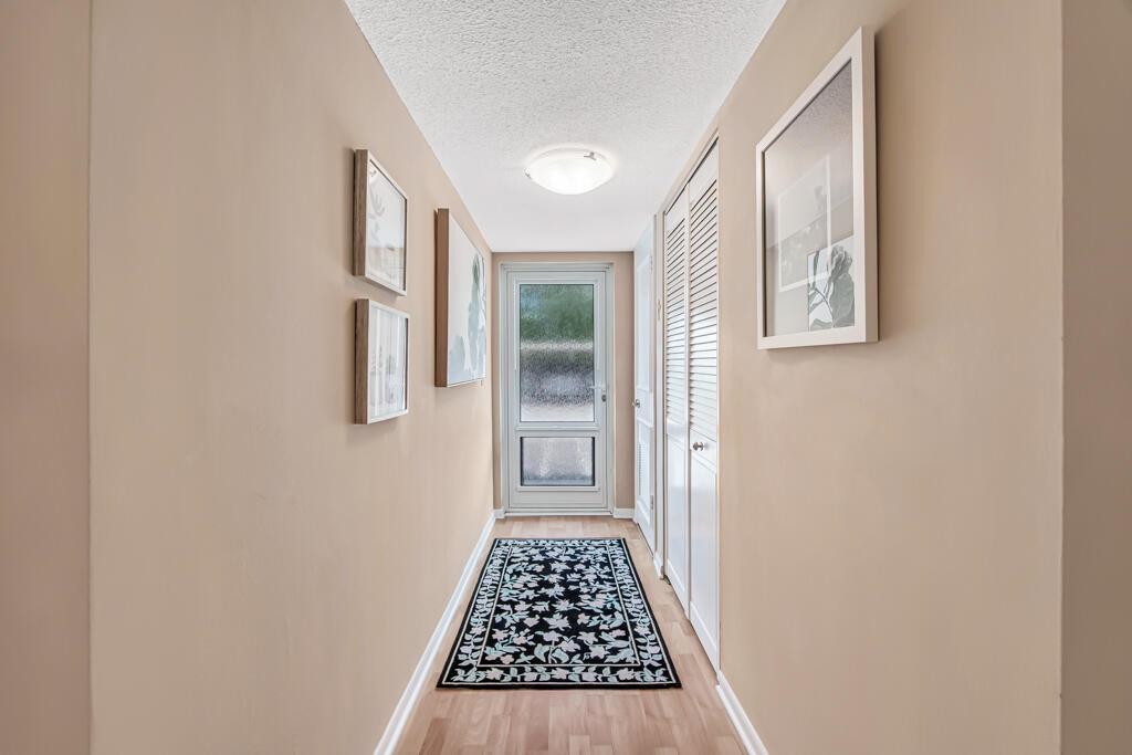 A hallway with light-colored walls, wood flooring, a patterned runner rug, and a glass door — 1910 S Ocean Boulevard # 112, Delray Beach FL 33483, DELRAY BEACH, FL