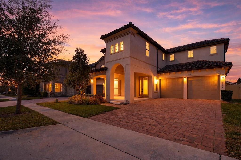 A two-story stucco house with a brick driveway and a three-car garage at sunset — 9218 HOLLISTON CREEK PLACE, WINTER GARDEN, FL