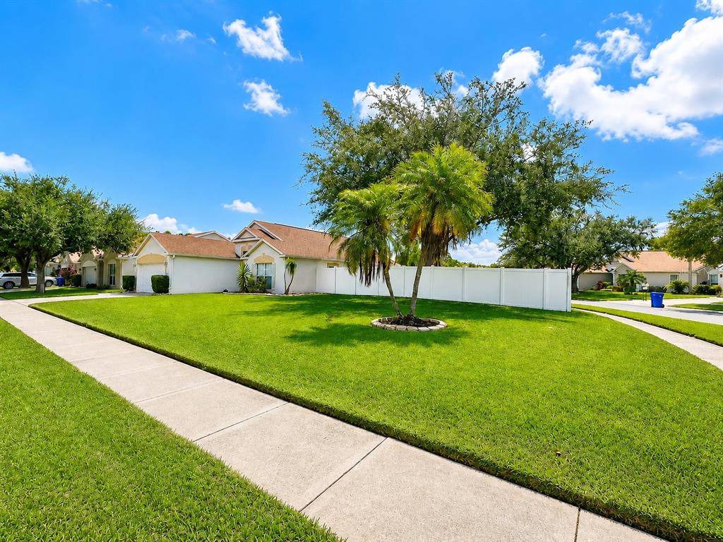 A single-story house with a white fence and a large lawn under a blue sky — 4201 PINE ISLE DRIVE, LUTZ, FL