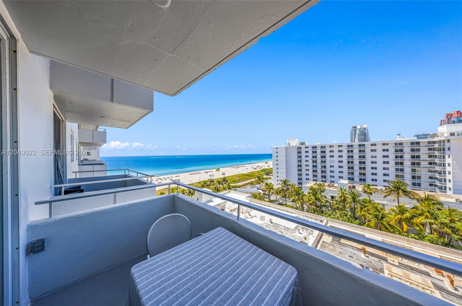 A balcony with a table and chairs overlooks the ocean, beach, and nearby buildings — 465 Ocean Dr # 1009, Miami Beach FL 33139, MIAMI BEACH, FL