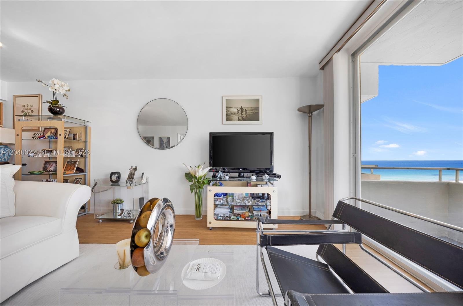 A living room features a television, a glass display shelf, and a balcony with ocean views — 465 Ocean Dr # 1009, Miami Beach FL 33139, MIAMI BEACH, FL