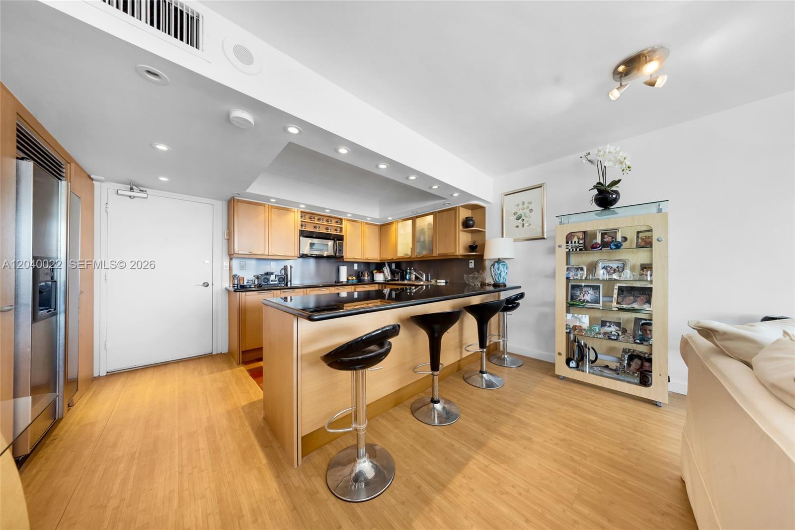 A kitchen features light wood cabinets, a black countertop, and three black bar stools — 465 Ocean Dr # 1009, Miami Beach FL 33139, MIAMI BEACH, FL