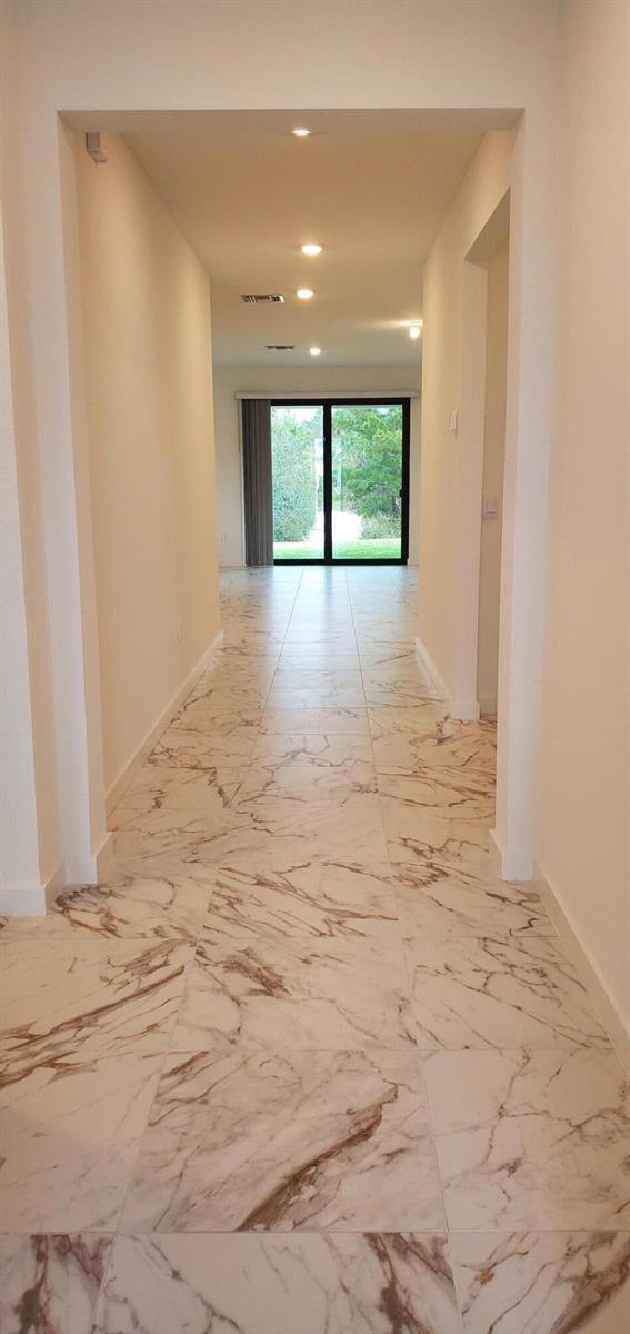 A hallway with white marble-look tile flooring leads to a glass sliding door — 1949 NE Ocean Dunes Drive, Jensen Beach FL 34957, JENSEN BEACH, FL