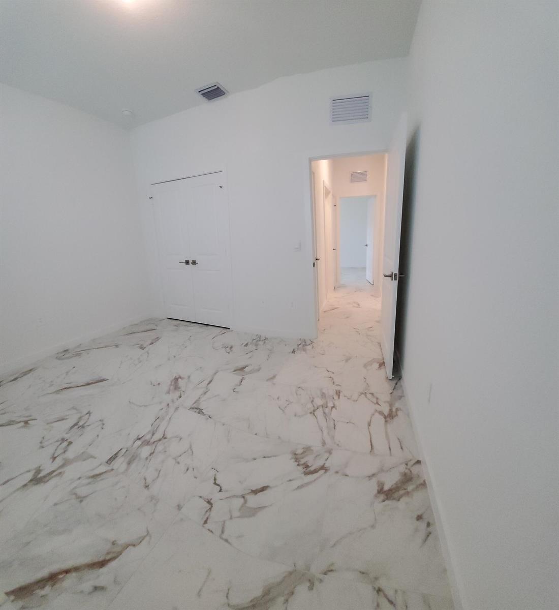 An empty room features white walls, a closet with double doors, and marble-patterned tile flooring — 1949 NE Ocean Dunes Drive, Jensen Beach FL 34957, JENSEN BEACH, FL