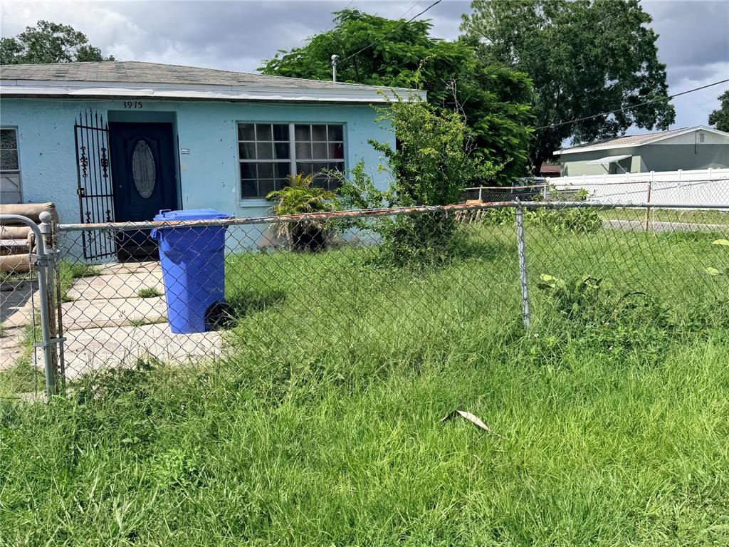 A light blue house with a chain-link fence and a blue trash bin in front — 3915 W BROAD STREET, TAMPA, FL