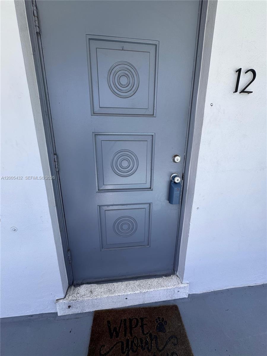 A gray front door with three square panels and a doormat labeled 12 — 3510 Harrison St # 12, Hollywood FL 33021, HOLLYWOOD, FL