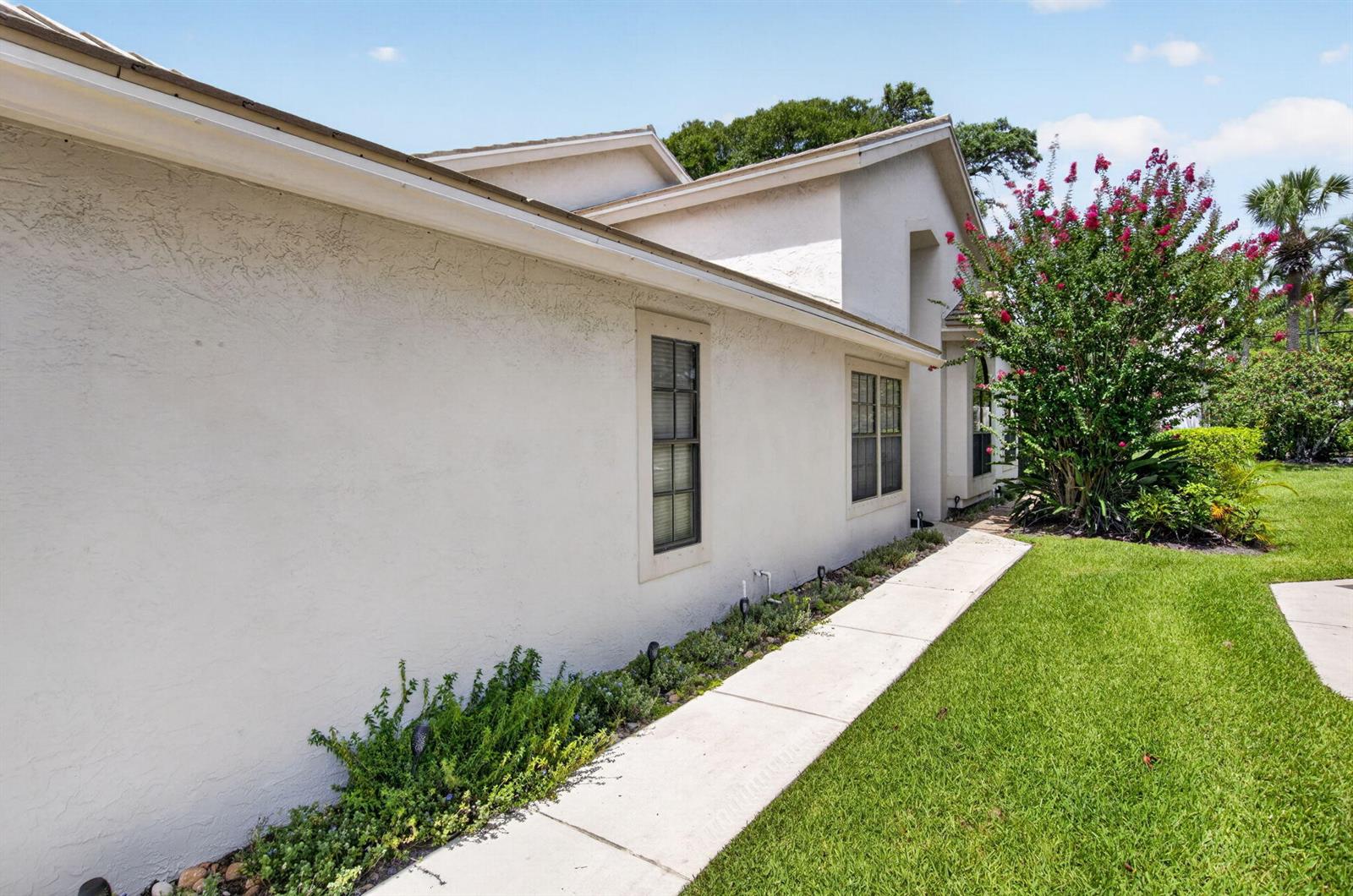 A side view of a stucco house with a concrete walkway and a flowering tree — 10984 Stafford Circle S, Boynton Beach FL 33436, BOYNTON BEACH, FL