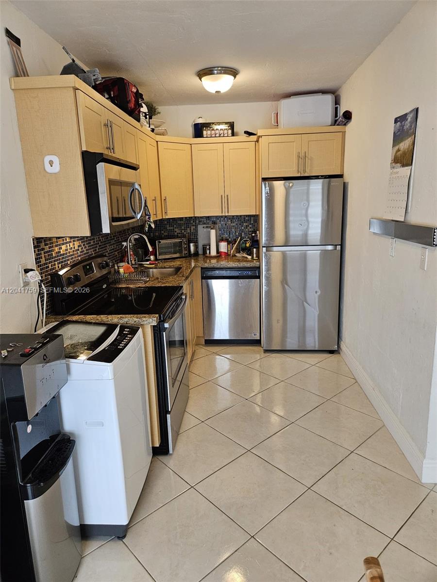 A kitchen features light wood cabinets, stainless steel appliances, a tiled backsplash, and diagonal flooring — 7400 Harding Ave # 22, Miami Beach FL 33141, MIAMI BEACH, FL