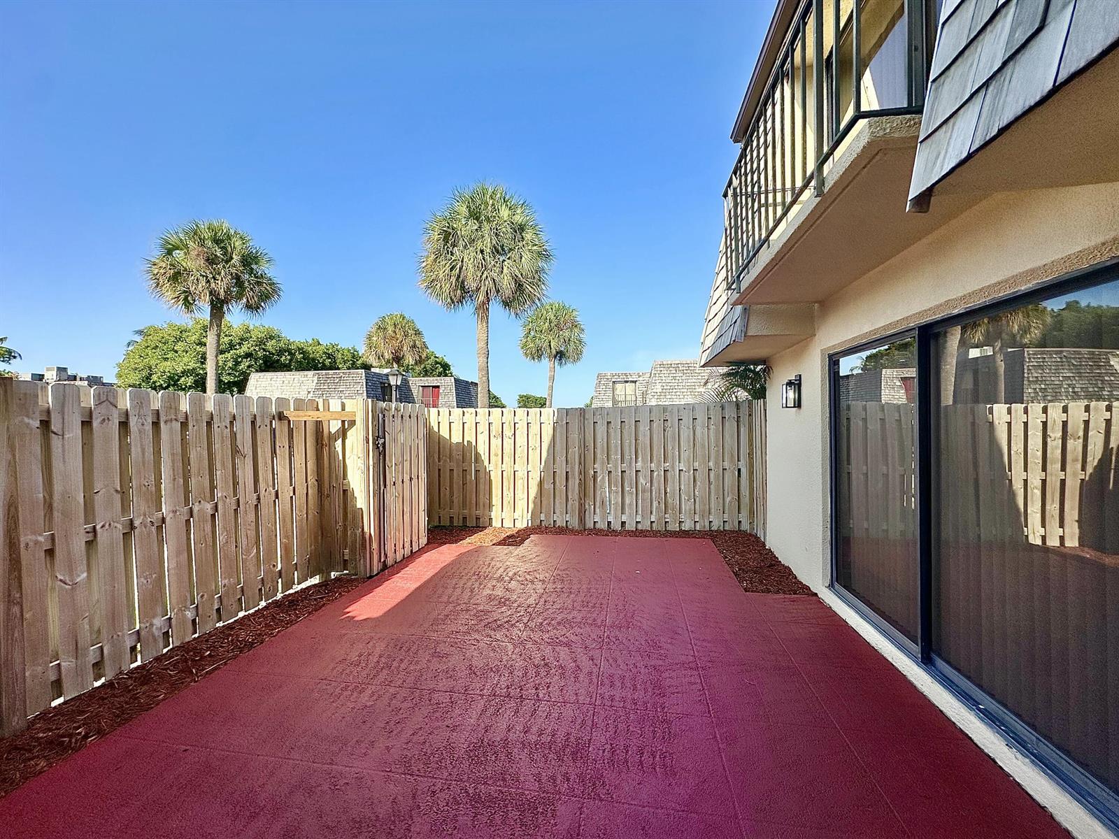 A red-painted patio sits beside a building with a sliding glass door and wooden fence — 251 Lake Arbor Drive, Palm Springs FL 33461, PALM SPRINGS, FL
