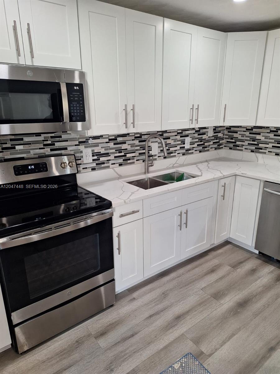A kitchen features white shaker cabinets, stainless steel appliances, and a gray-and-white tiled backsplash — 6328 SW 20th St, Miramar FL 33023, MIRAMAR, FL