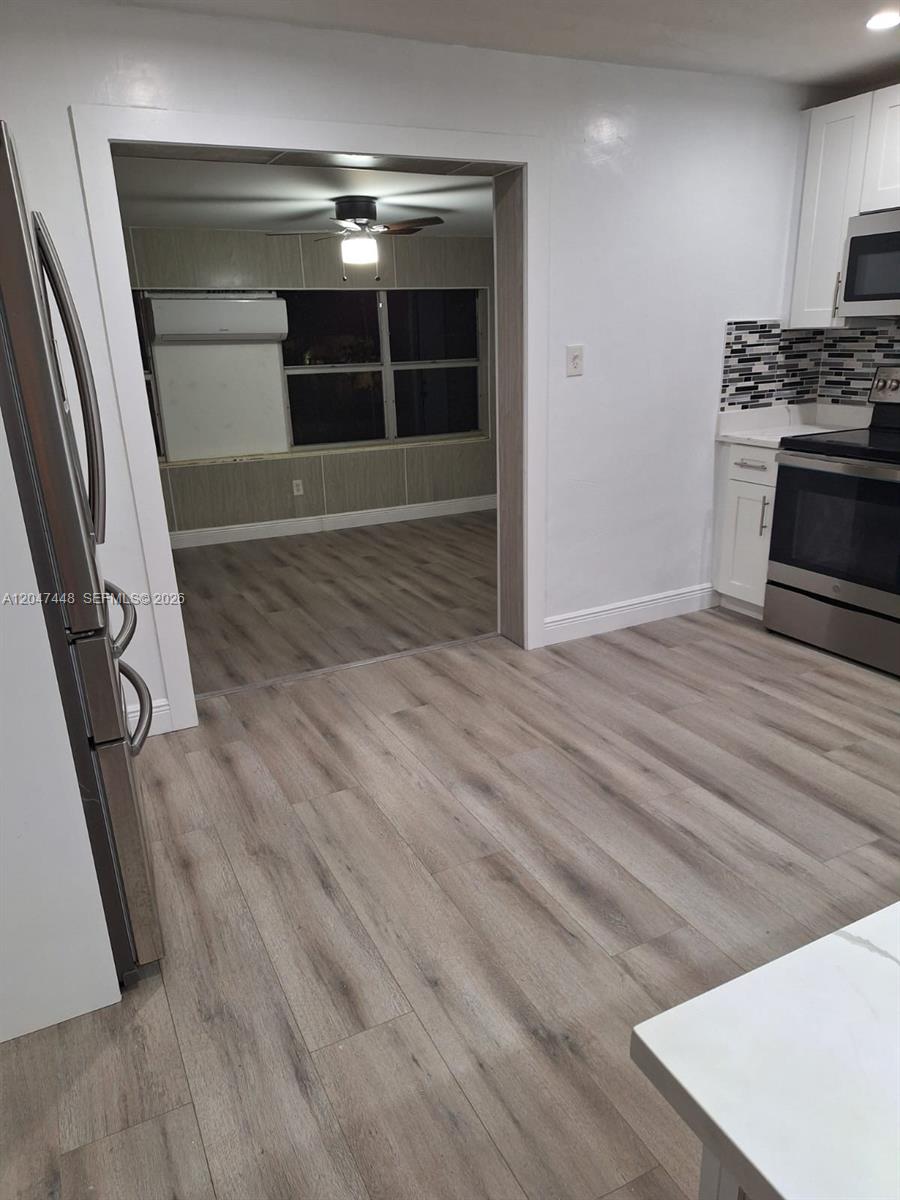 A kitchen with stainless steel appliances and wood-look flooring opens into an adjacent living area — 6328 SW 20th St, Miramar FL 33023, MIRAMAR, FL