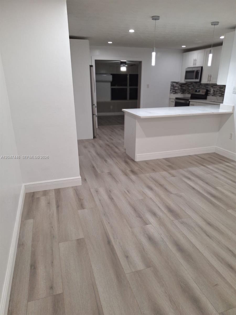 This interior view shows a kitchen with a white breakfast bar and light wood flooring — 6328 SW 20th St, Miramar FL 33023, MIRAMAR, FL