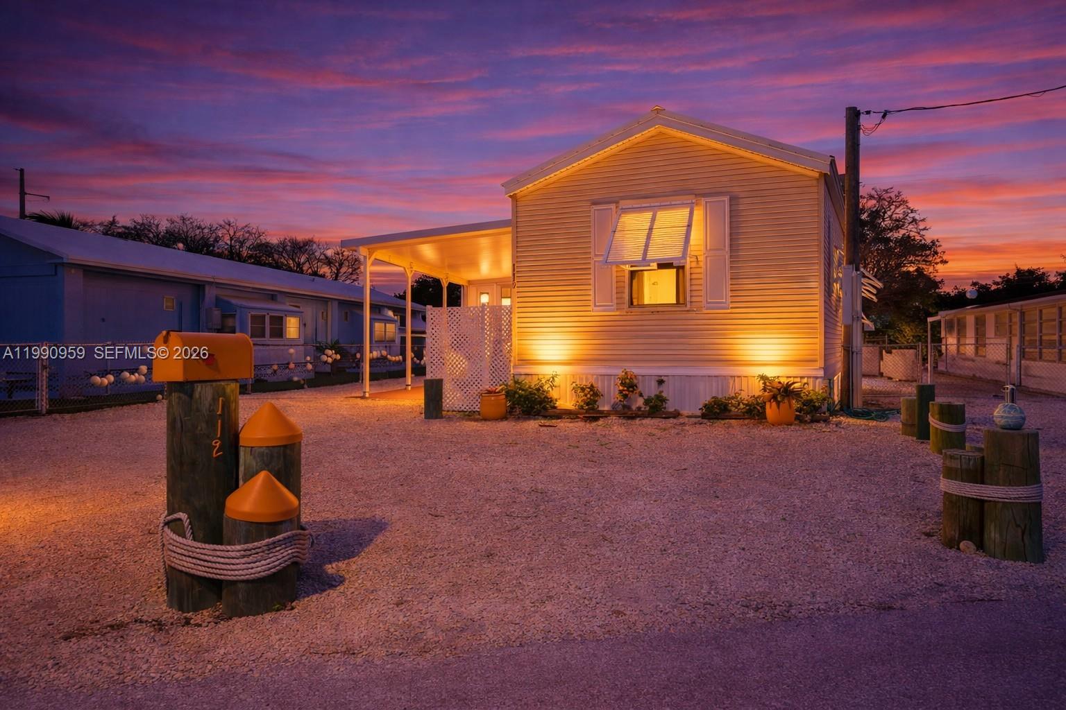 A yellow mobile home with a gravel driveway and nautical-themed posts at sunset — 112 Tweedy Pie Ter, Key Largo FL 33037, KEY LARGO, FL
