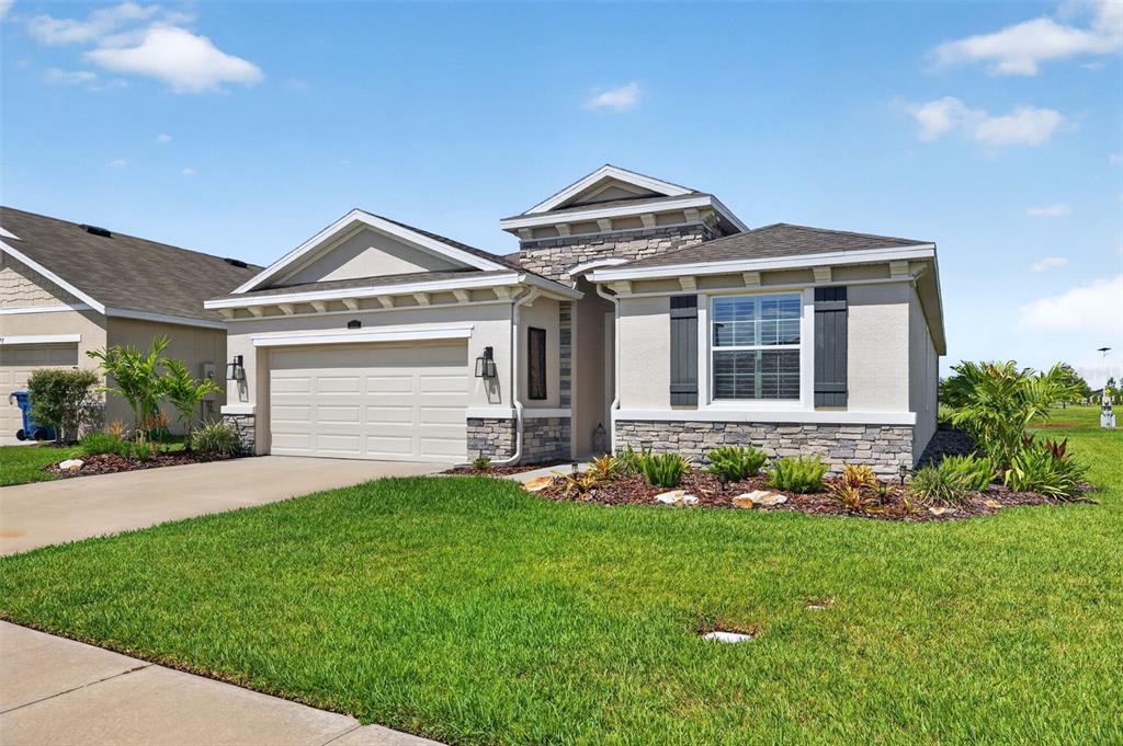 A single-story suburban house with a stone facade, beige stucco, and a two-car garage — 8955 BOWER BASS CIRCLE, WESLEY CHAPEL, FL