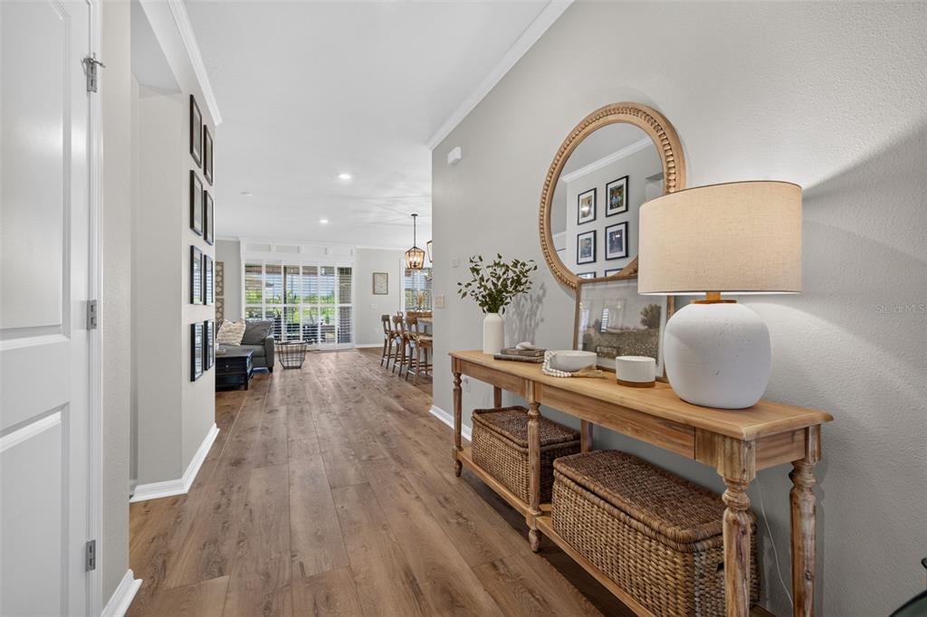 A hallway features wood-look flooring, a wooden console table with wicker baskets, and a round mirror — 8955 BOWER BASS CIRCLE, WESLEY CHAPEL, FL