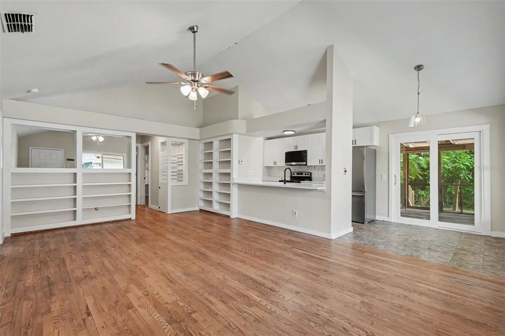 A living room with wood floors, built-in shelving, and an open kitchen with white cabinets — 3751 MACKENZIE COURT, PALM HARBOR, FL