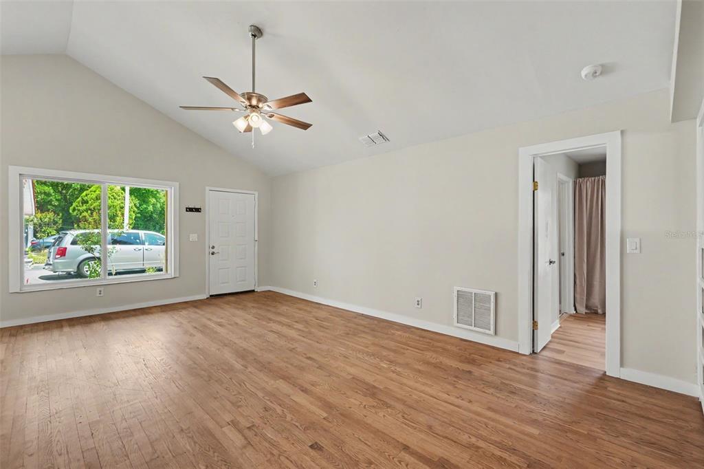 An empty living room features hardwood floors, a vaulted ceiling with a fan, and a doorway — 3751 MACKENZIE COURT, PALM HARBOR, FL