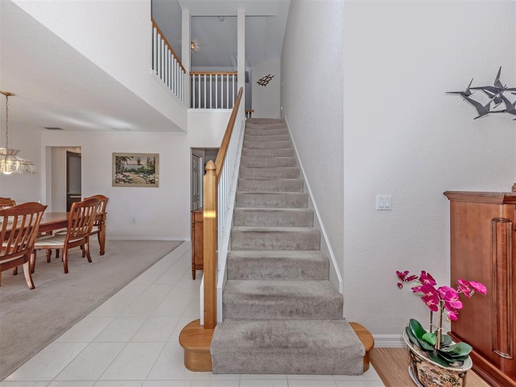 A carpeted staircase with a wooden railing leads to a second-floor landing in a foyer — 897 COLONIAL ROAD, VENICE, FL