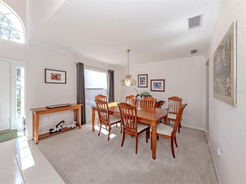 A dining room features a wooden table with six chairs, a chandelier, and carpeted flooring — 897 COLONIAL ROAD, VENICE, FL